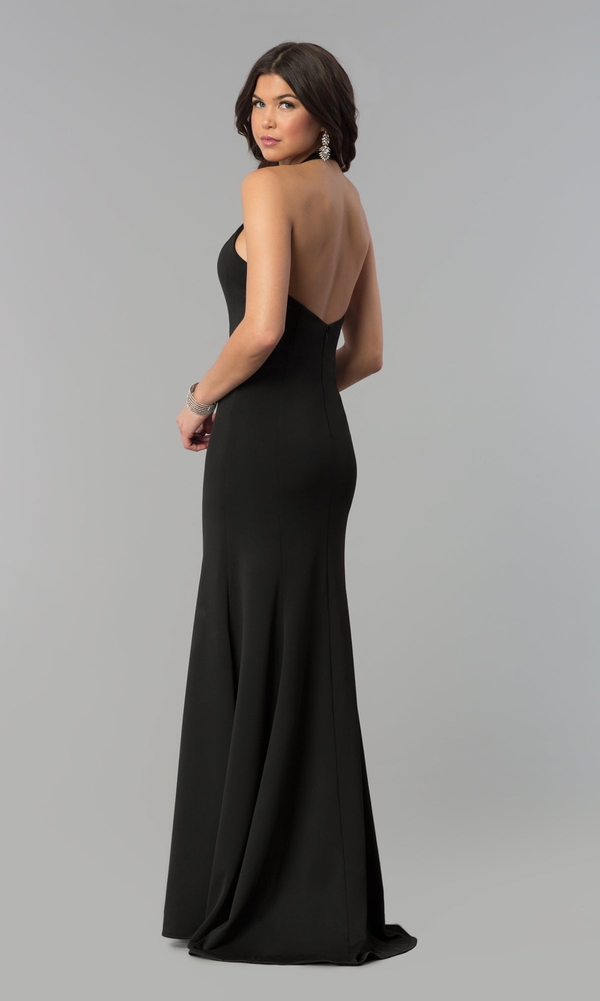 Woman in a fitted Halter V-Neck Long Jersey Formal Prom Dress 8262, standing and looking over her shoulder against a plain gray background.